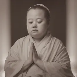 A close-up photograph of a person with Down syndrome engaged in a peaceful and focused meditation practice, with soft light illuminating their serene expression.